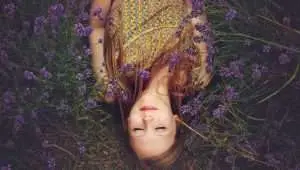 young woman with a red long hair laying in the nature suranded by violet color flowers